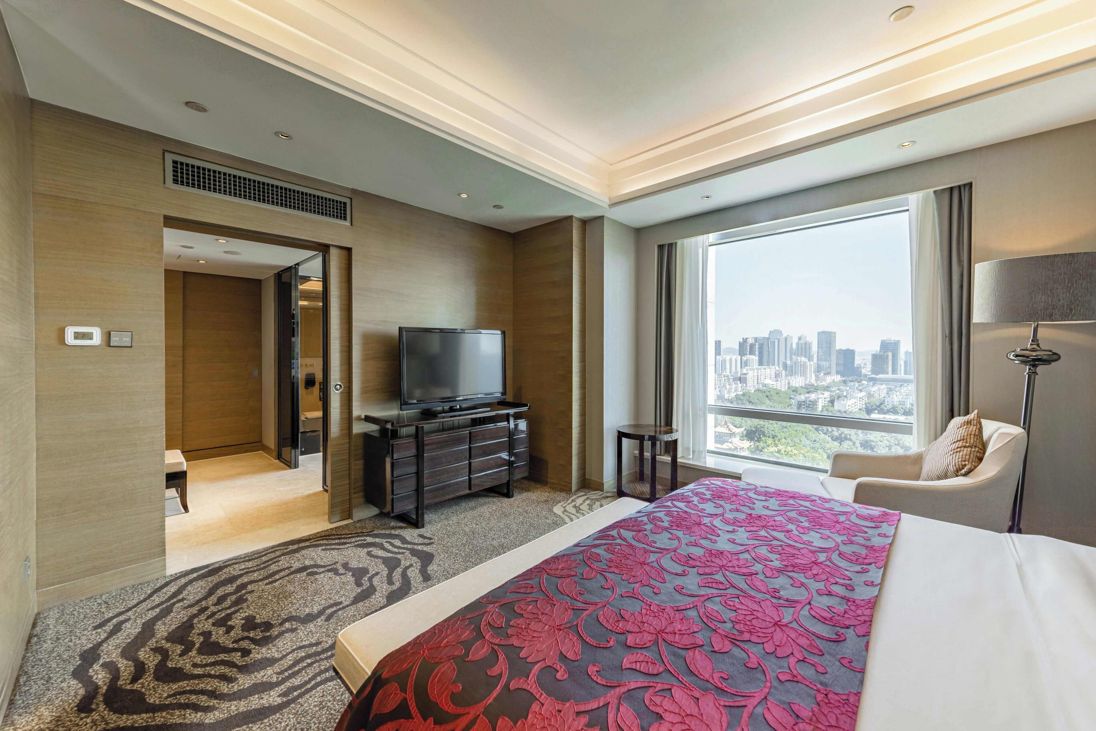 A hotel room with a large bed, a TV on a dresser, a city view, and a modern design.