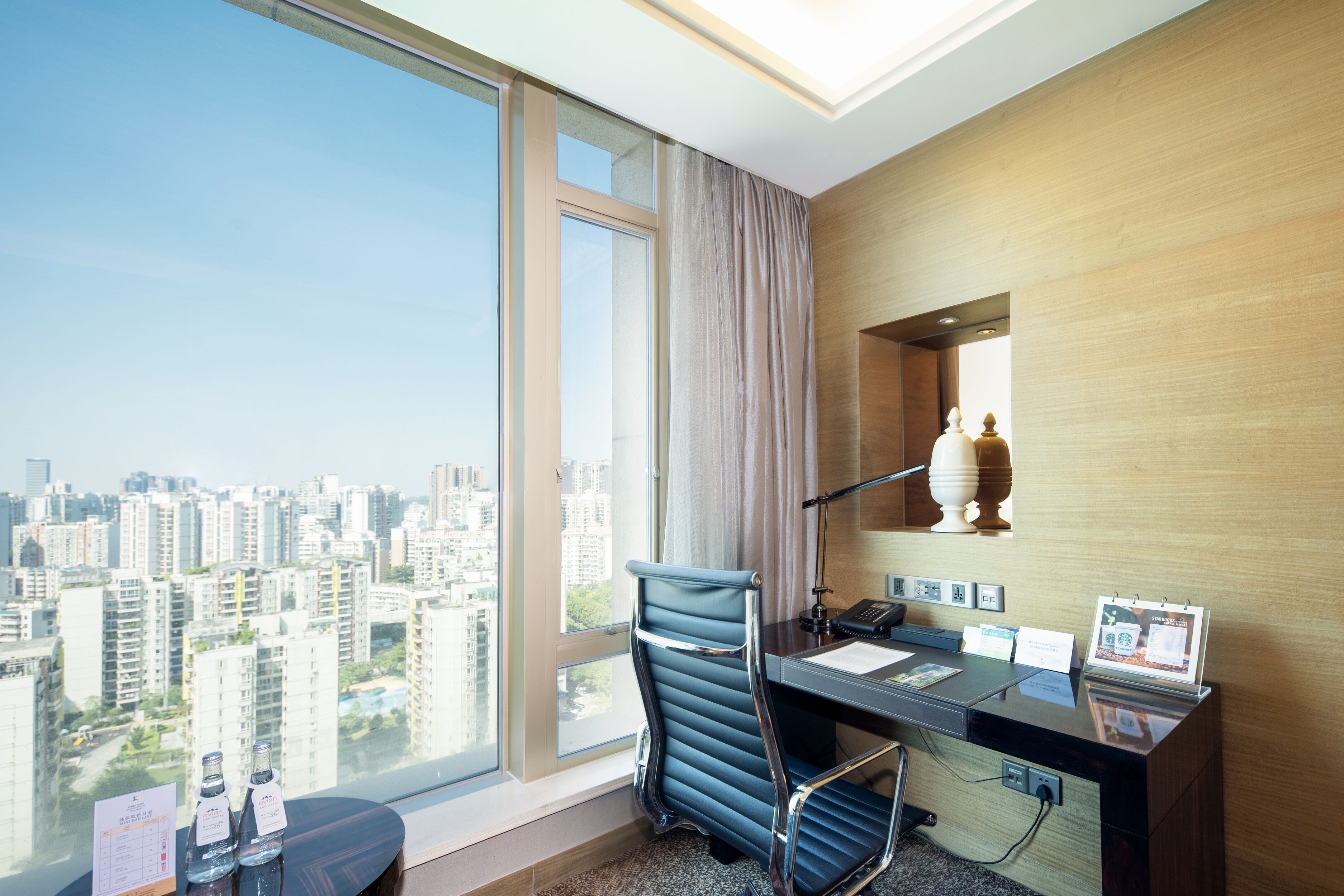 Una habitación de hotel moderna con un gran ventanal, un escritorio con computadora y una silla.