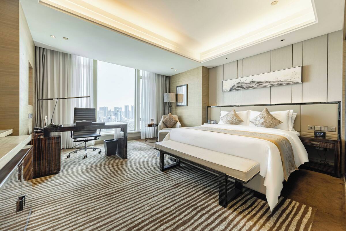 A modern hotel room with a large bed, a desk, and a view of the city.