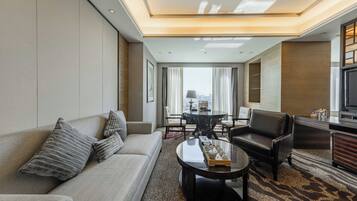A modern hotel room with a sofa, armchair, and a dining table with chairs.