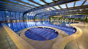 Una gran piscina interior con una zona circular central, rodeada por un muro curvo y un techo de cristal.