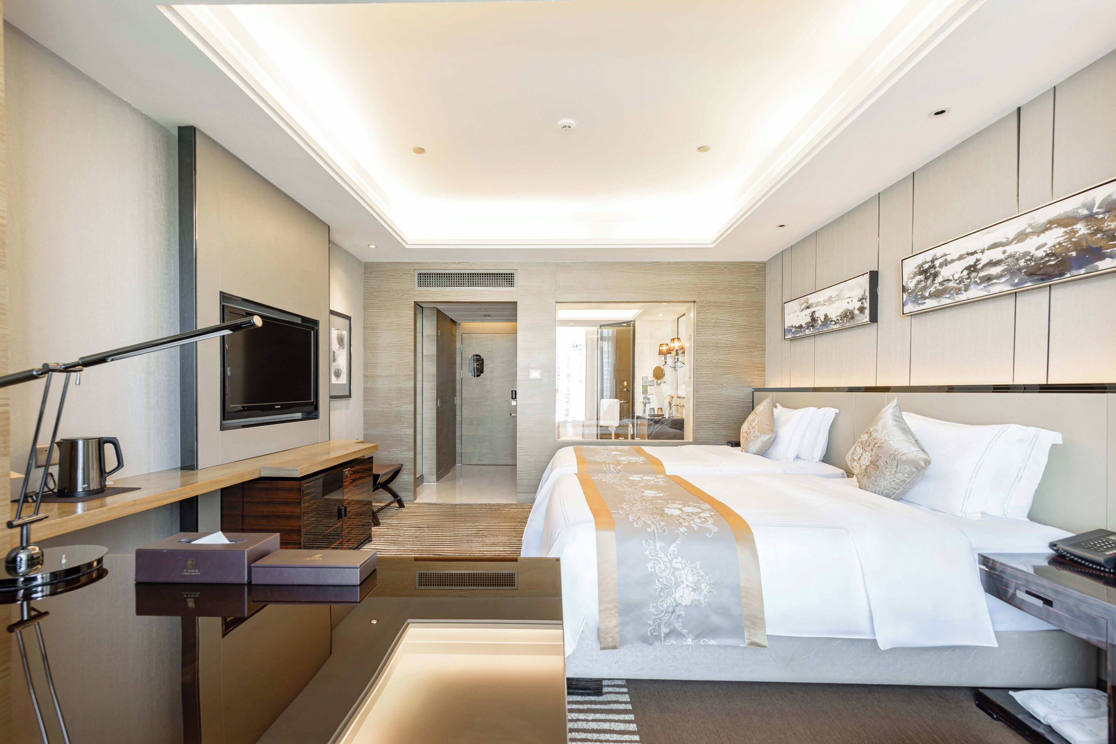 A modern hotel room with a large bed, a desk with a computer, a flat-screen TV, and a bathroom visible through an open door.