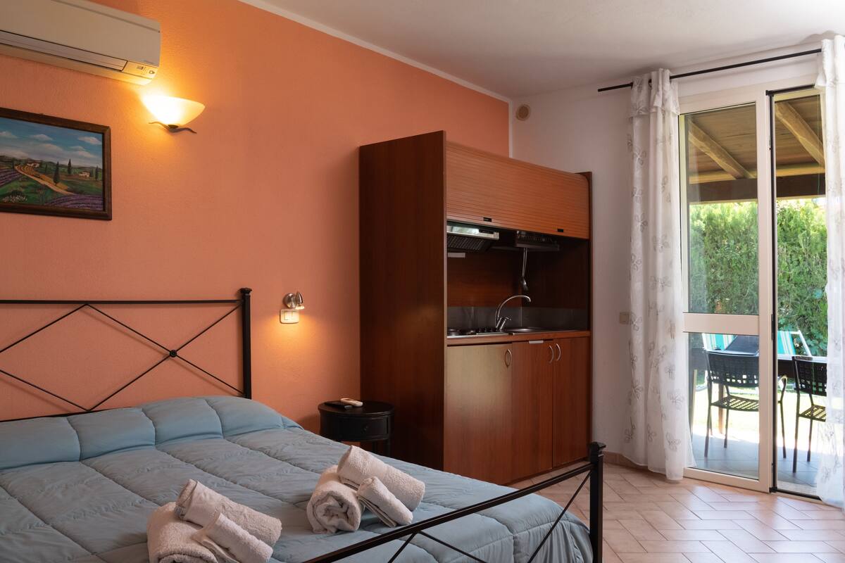Une chambre à coucher comprenant un lit, une table de chevet, un tableau, une armoire en bois et une porte-fenêtre coulissante donnant sur un espace extérieur.