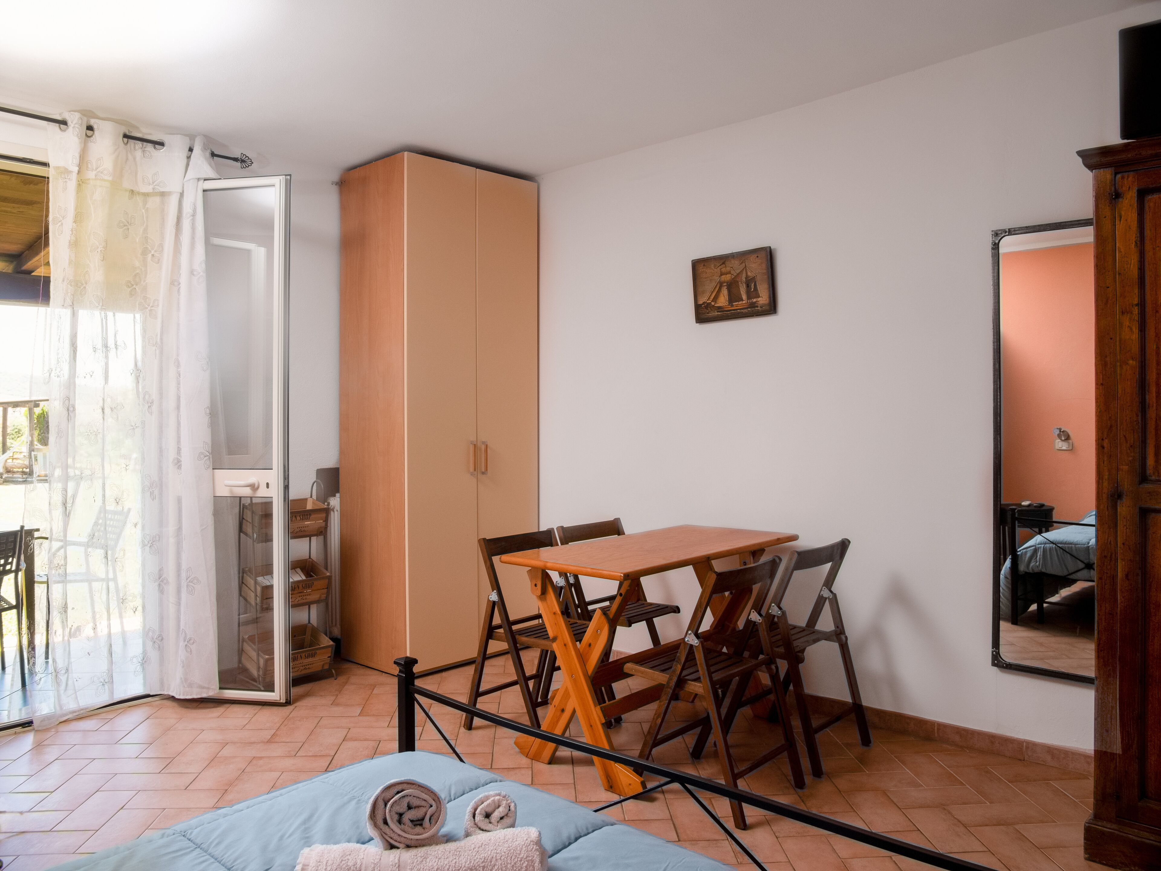 A room with a bed, a table, chairs, a wardrobe, and a window with curtains.
