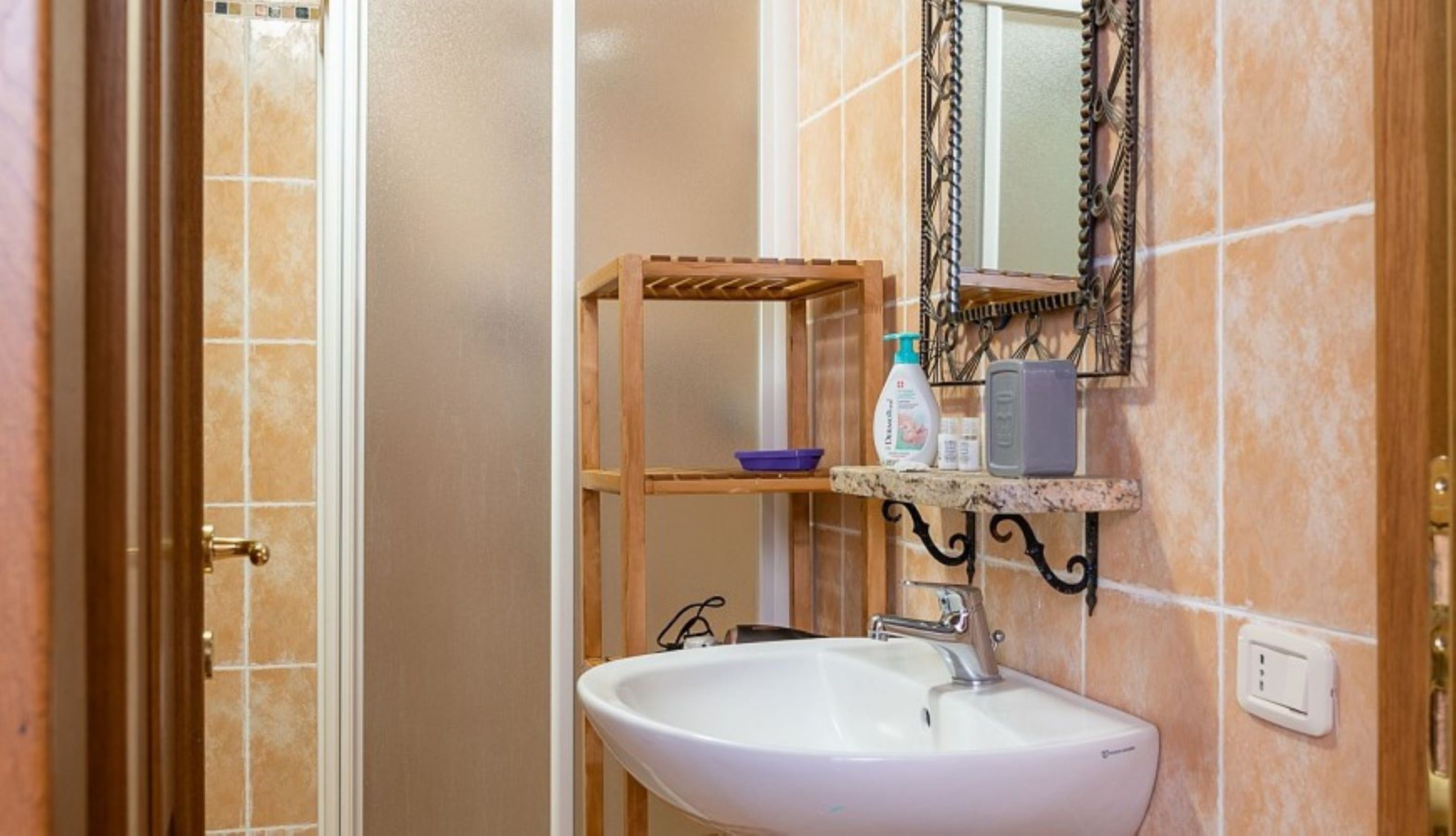 A bathroom with a white sink, a mirror, a shelf with toiletries, and a wooden rack.