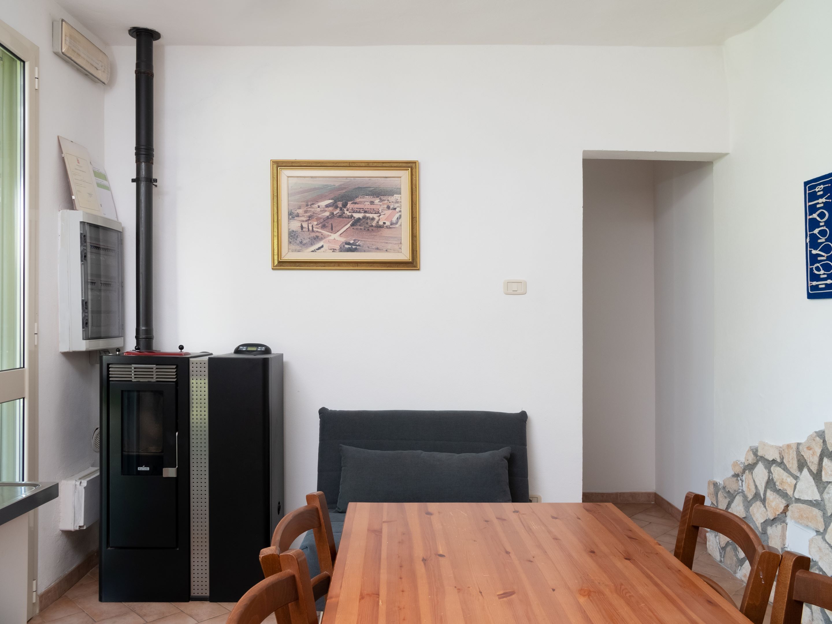 Un comedor con una mesa y sillas de madera, un refrigerador negro, un calentador fijado a la pared y un cuadro con un paisaje.