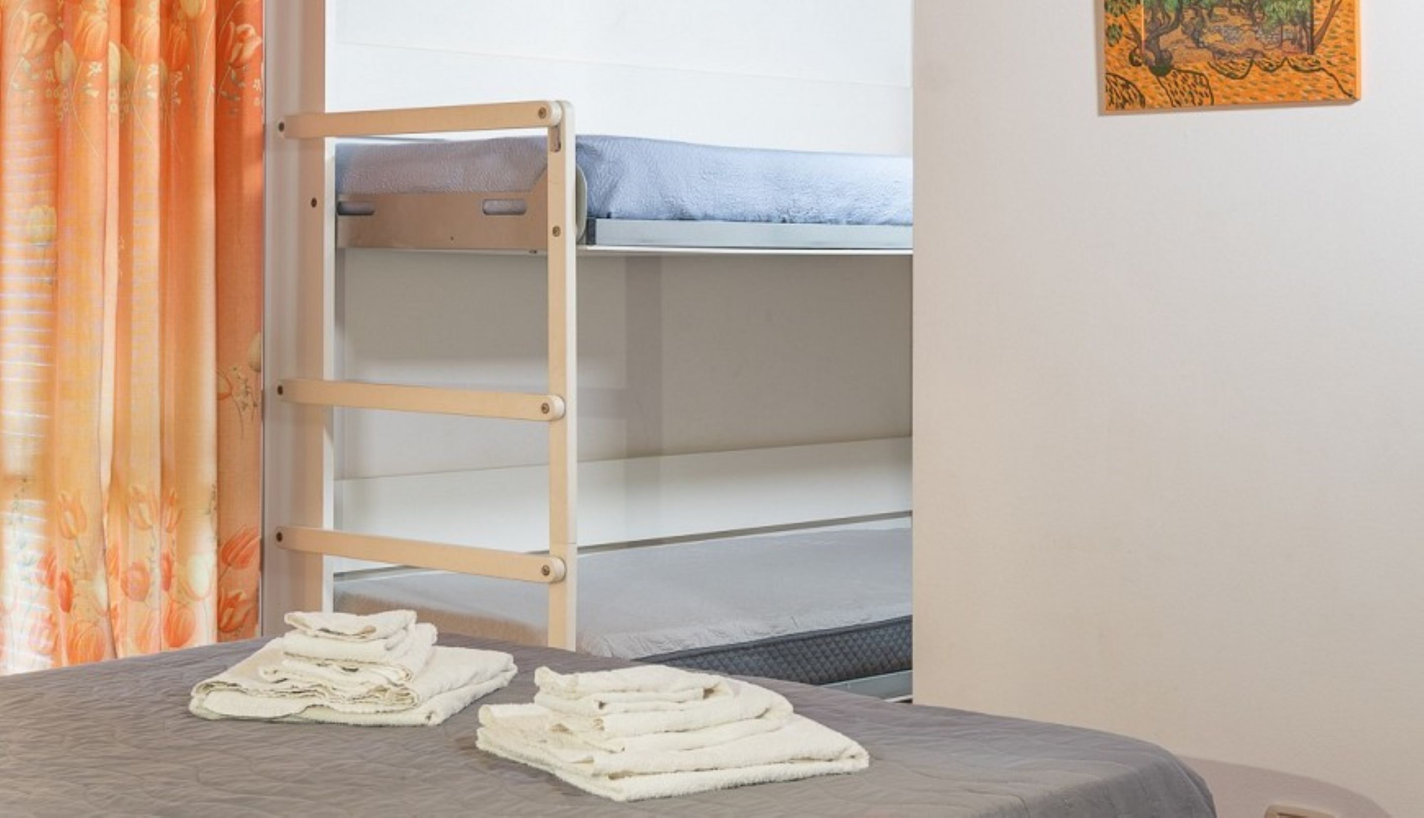 A bunk bed with a ladder, a bed with a gray blanket, and a folded white towel on the floor.