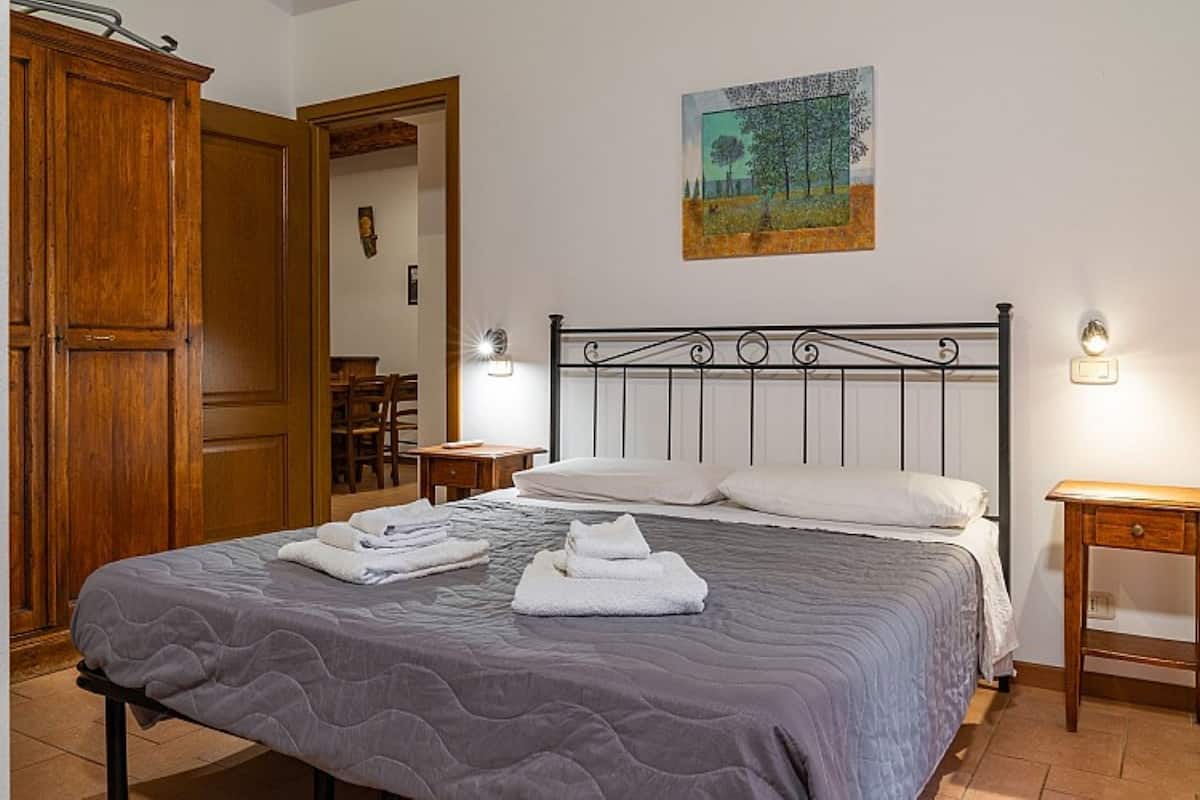 Un lit bien fait, recouvert d’une couverture grise, une armoire en bois et un tableau accroché au mur.