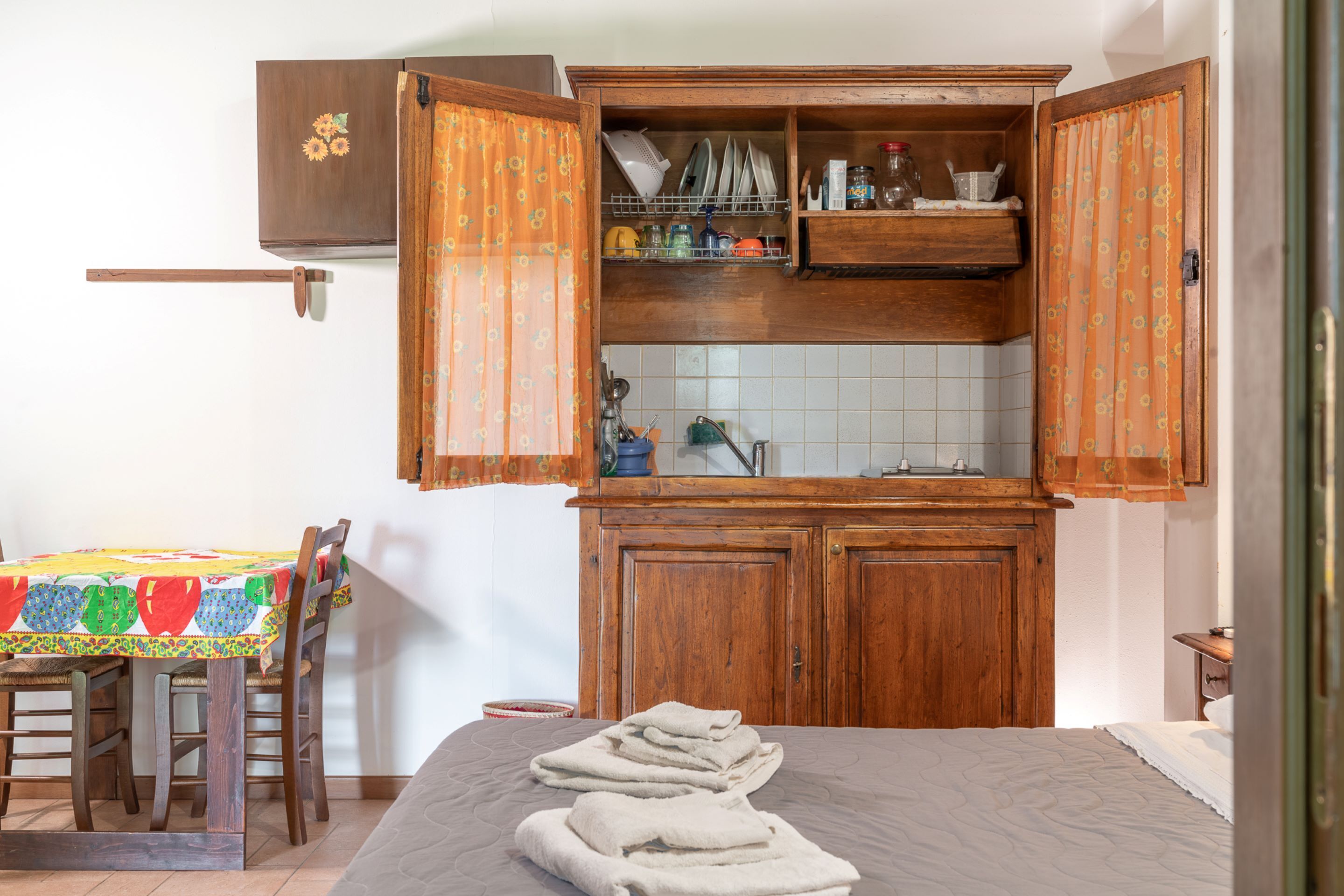Una habitació amb llit, taula amb estovell de colors, armaris de fusta i un salvasalls de rajola.