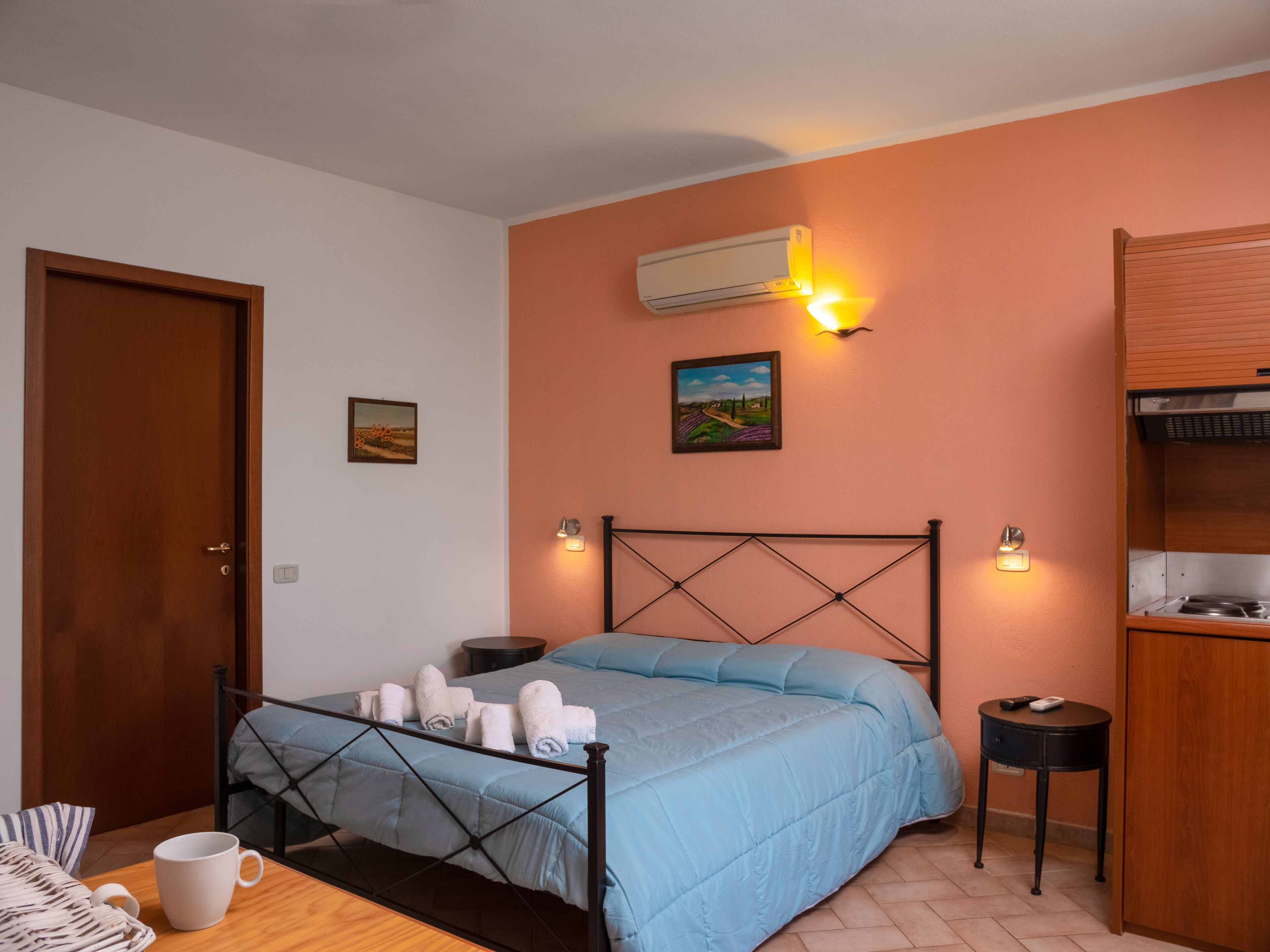 A bedroom with a bed, a bedside table, a nightstand, an air conditioning unit, and a wall-mounted shelf.