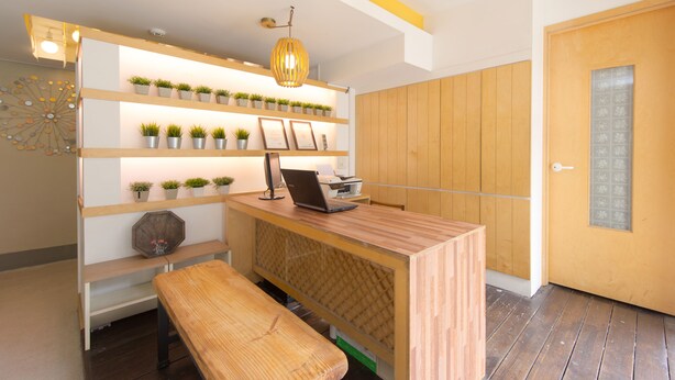 A reception desk with a laptop, shelves with potted plants, a bench, and a wooden door. - Travel Monster (Seoul)