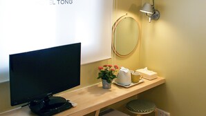 A hotel room with a desk, a computer, a mirror, a small stool, and a bedside table with a lamp. - Travel Monster (Seoul)