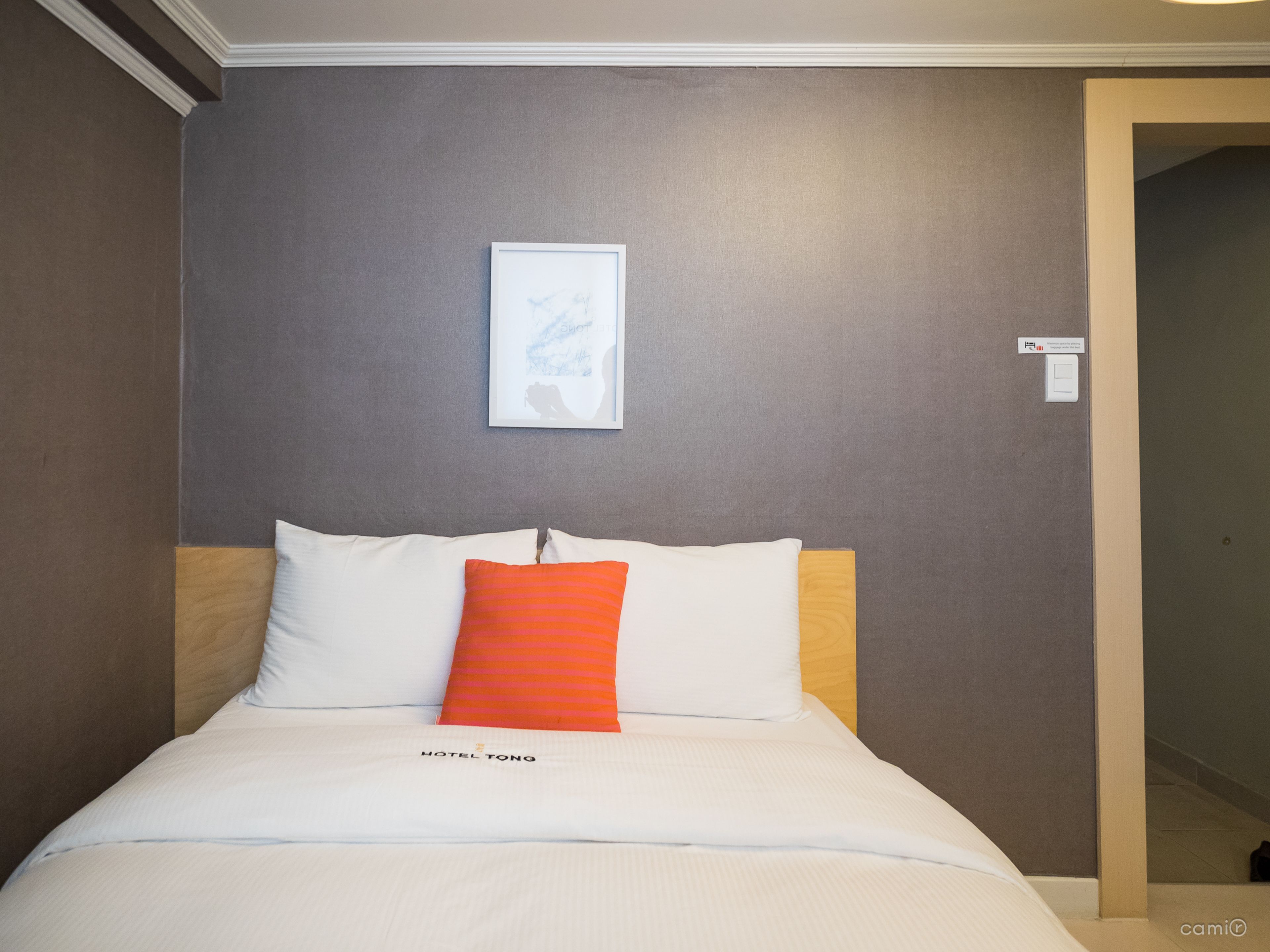 A hotel room with a bed, a framed picture on the wall, and a sign indicating the room number.