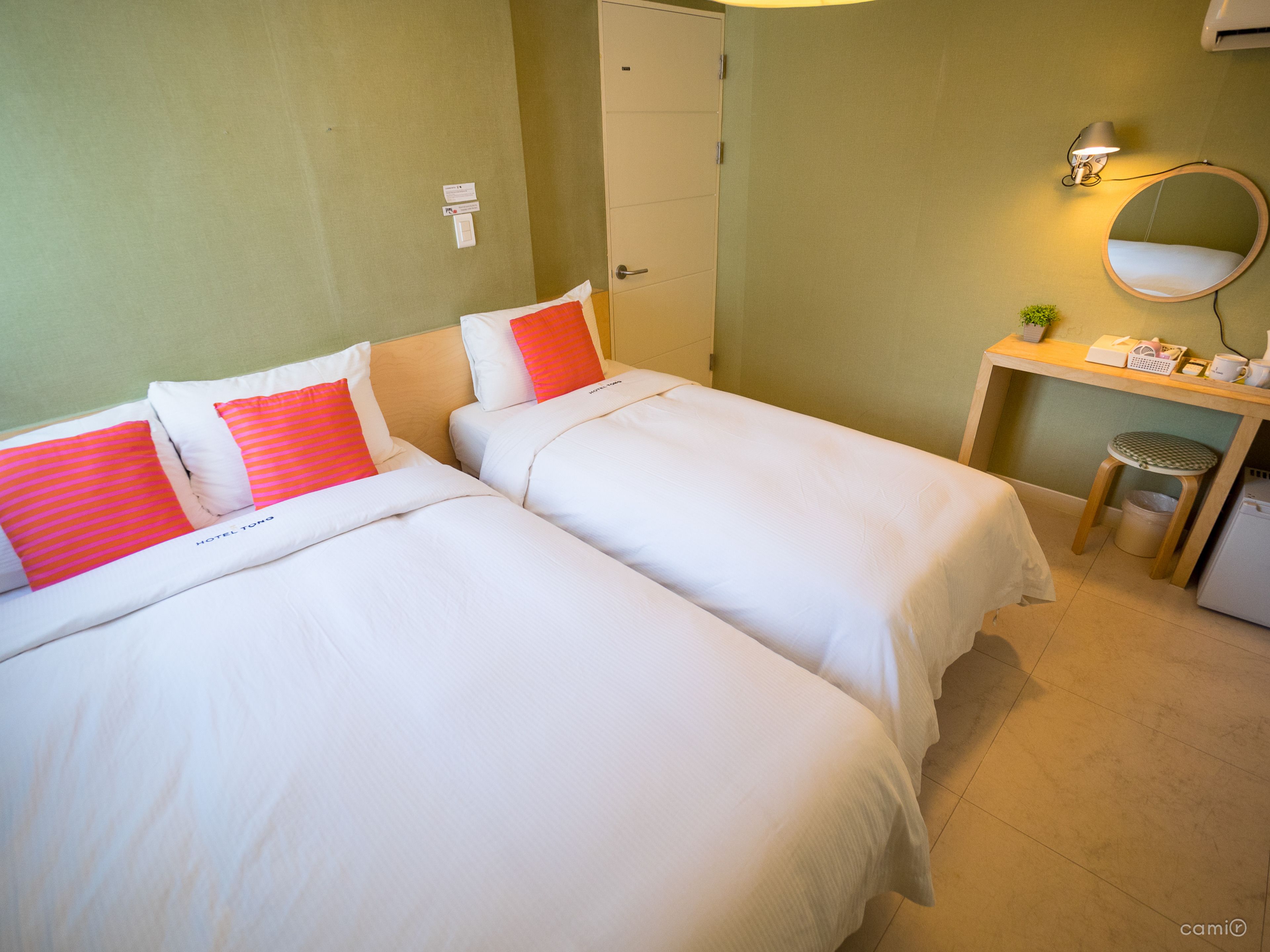 A hotel room with two beds, a desk, a mirror, and a trash bin.