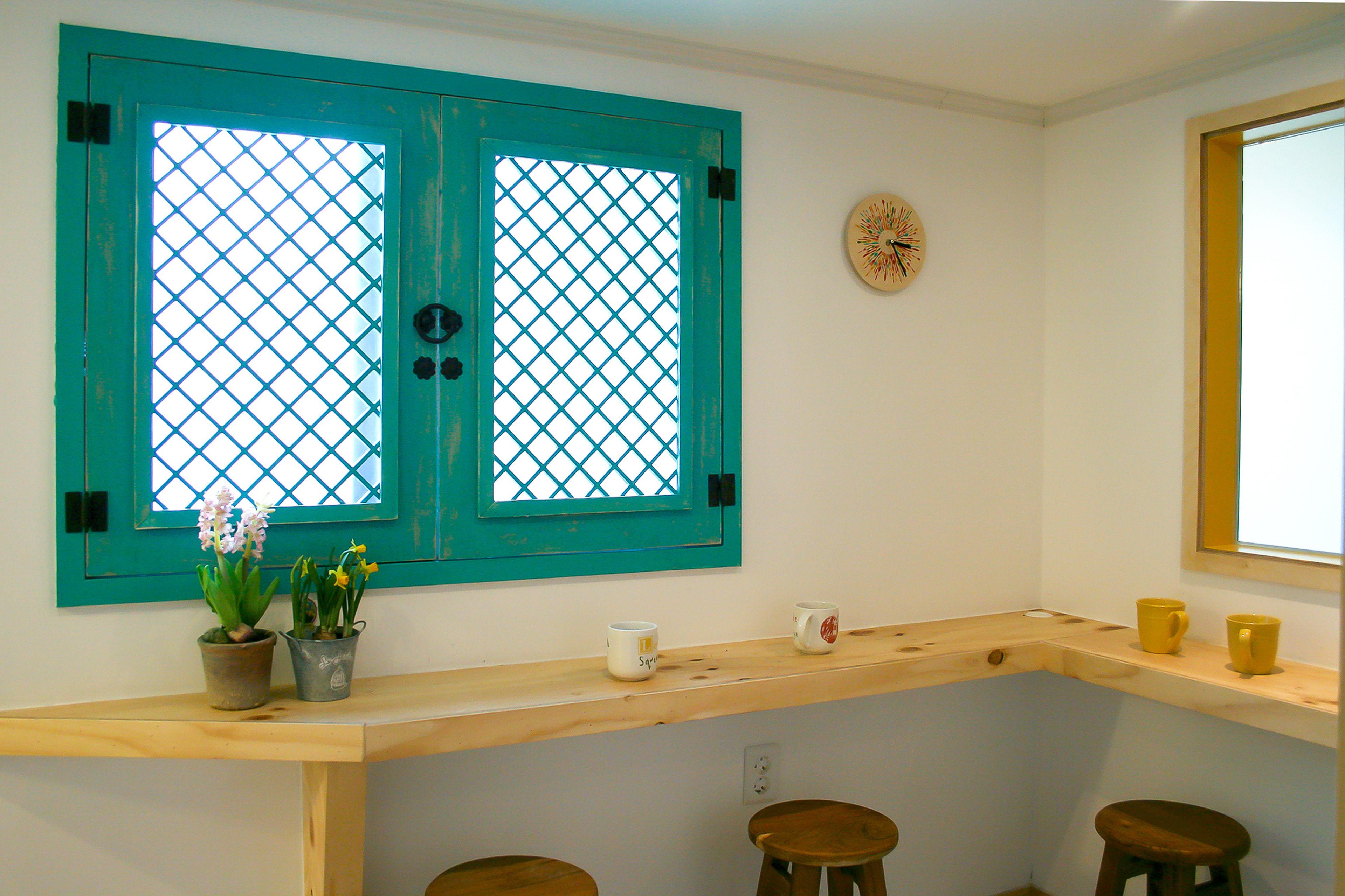 Una habitación con una puerta verde azulada, un ventanal pequeño, un reloj de pared y una encimera de madera con taburetes.