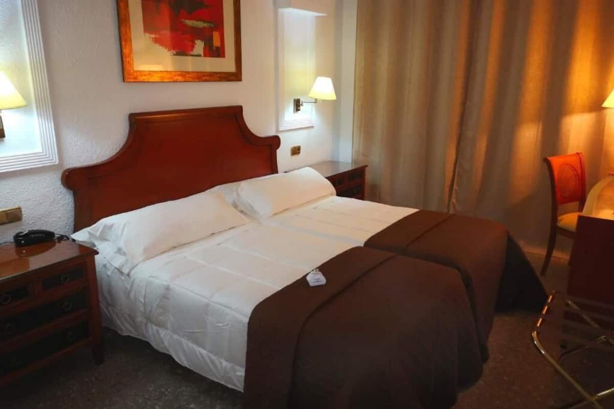 A hotel room with a large bed, two bedside tables, a chair, and a painting on the wall.