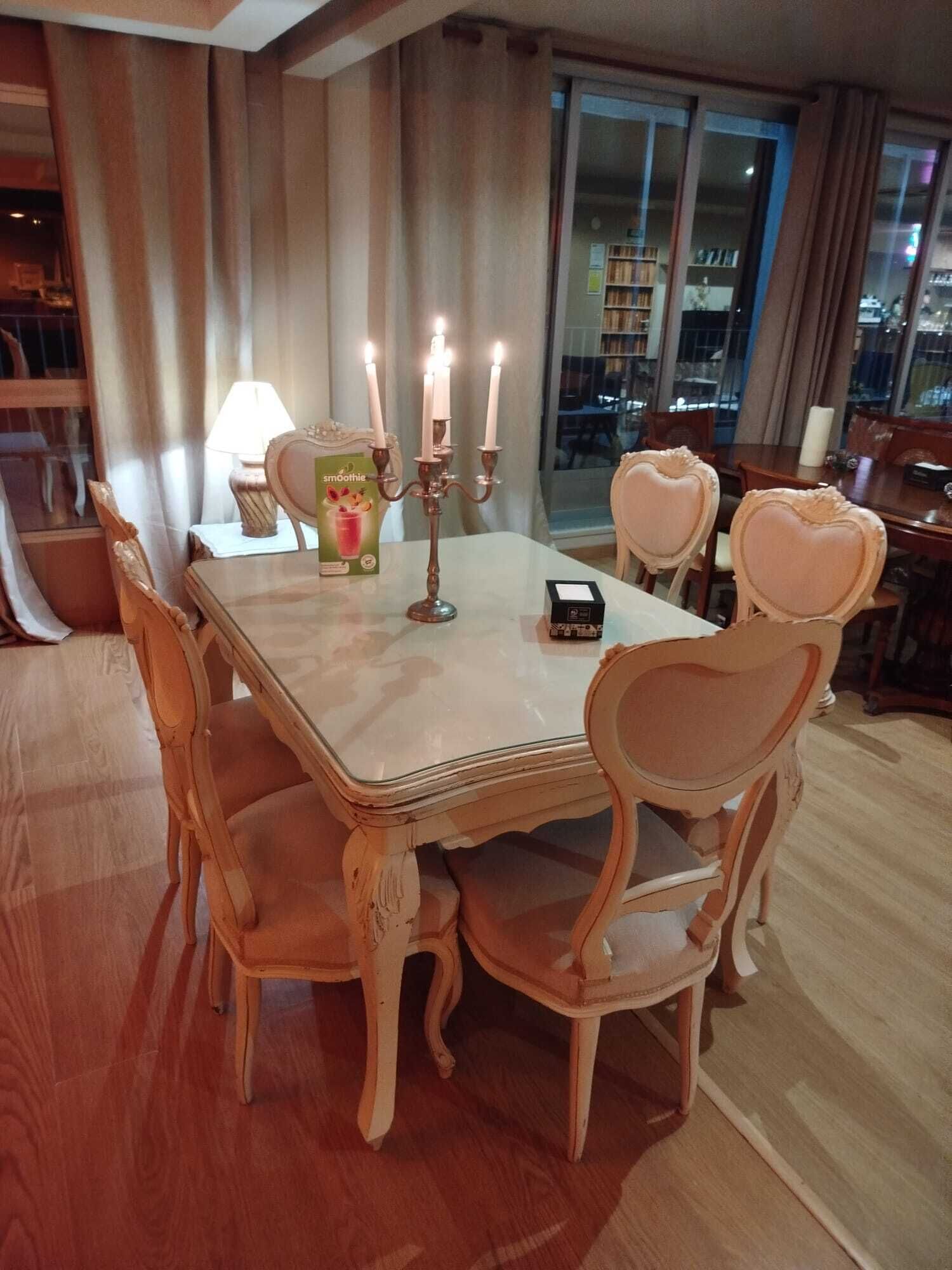 Un comedor con una mesa dispuesta para seis personas, rodeada de sillas con forma de corazón, un candelabro con velas encendidas y una lámpara.