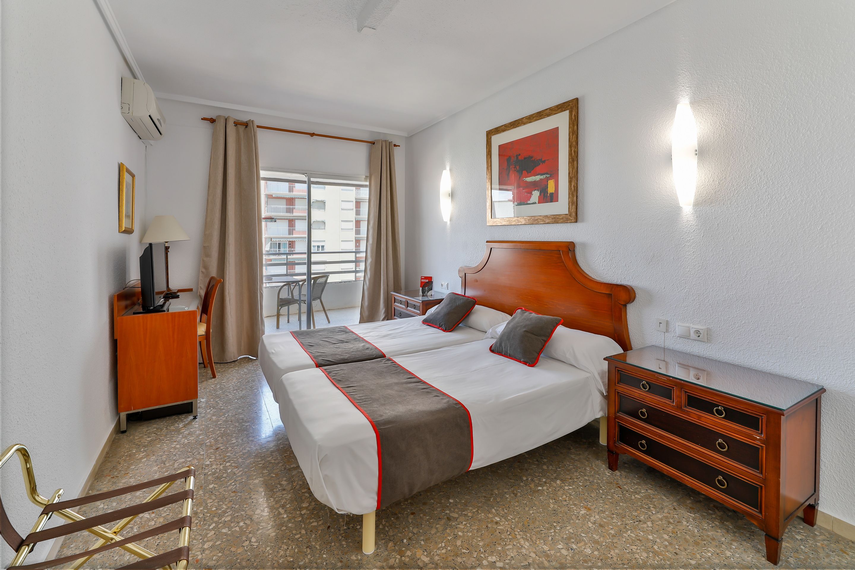 A hotel room with a bed, a dresser, a desk, a chair, and a window with a view of buildings.