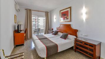 A hotel room with a bed, a dresser, a desk, a chair, and a window with a view of buildings.