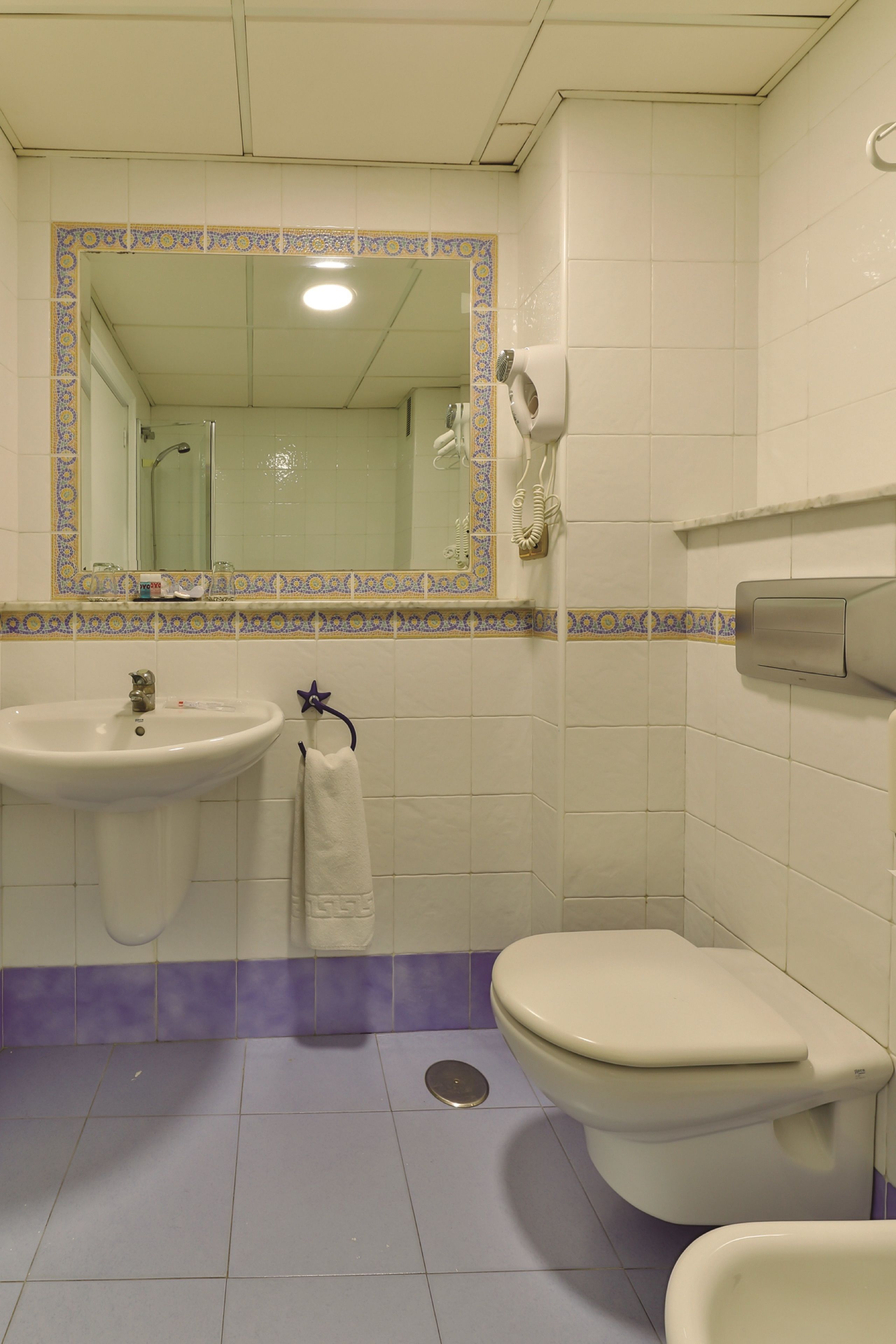 A bathroom with a sink, toilet, and a mirror with a decorative border.