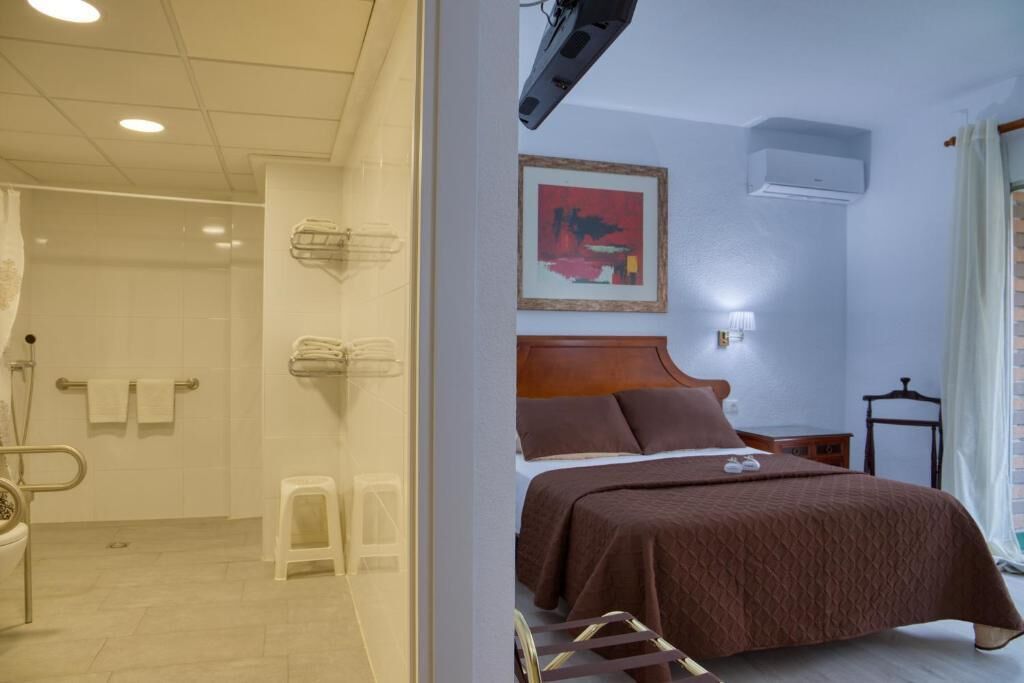 Habitación de hotel con cama, mesita de noche, aire acondicionado instalado en la pared y una ventana con cortinas.
