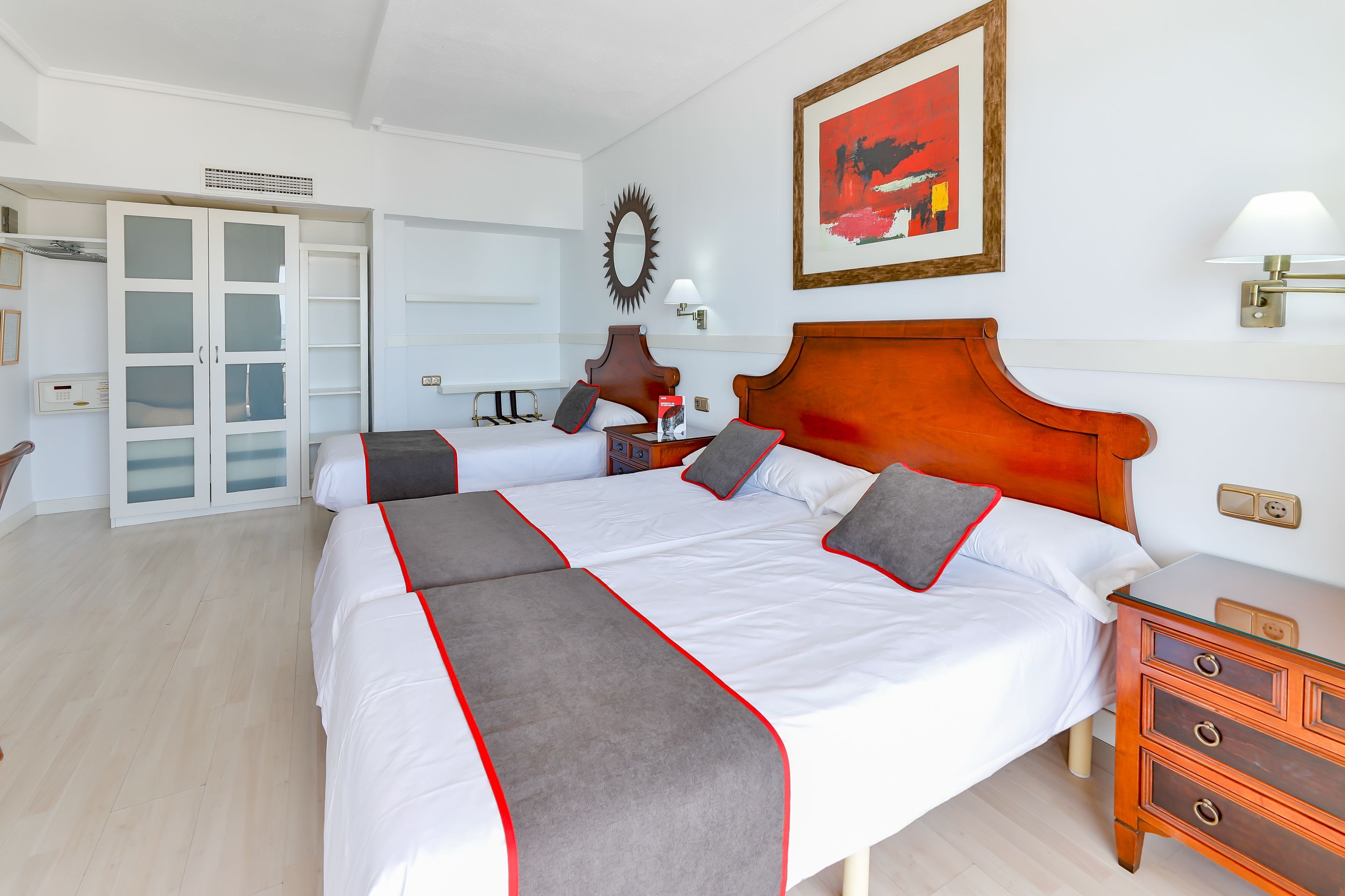 A hotel room with a large bed, a wooden nightstand, a desk, and a wardrobe with glass doors.