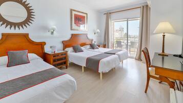 Habitación de hotel con dos camas, un escritorio, una silla, un balcón con vistas y un adorno con forma de sol en la pared.