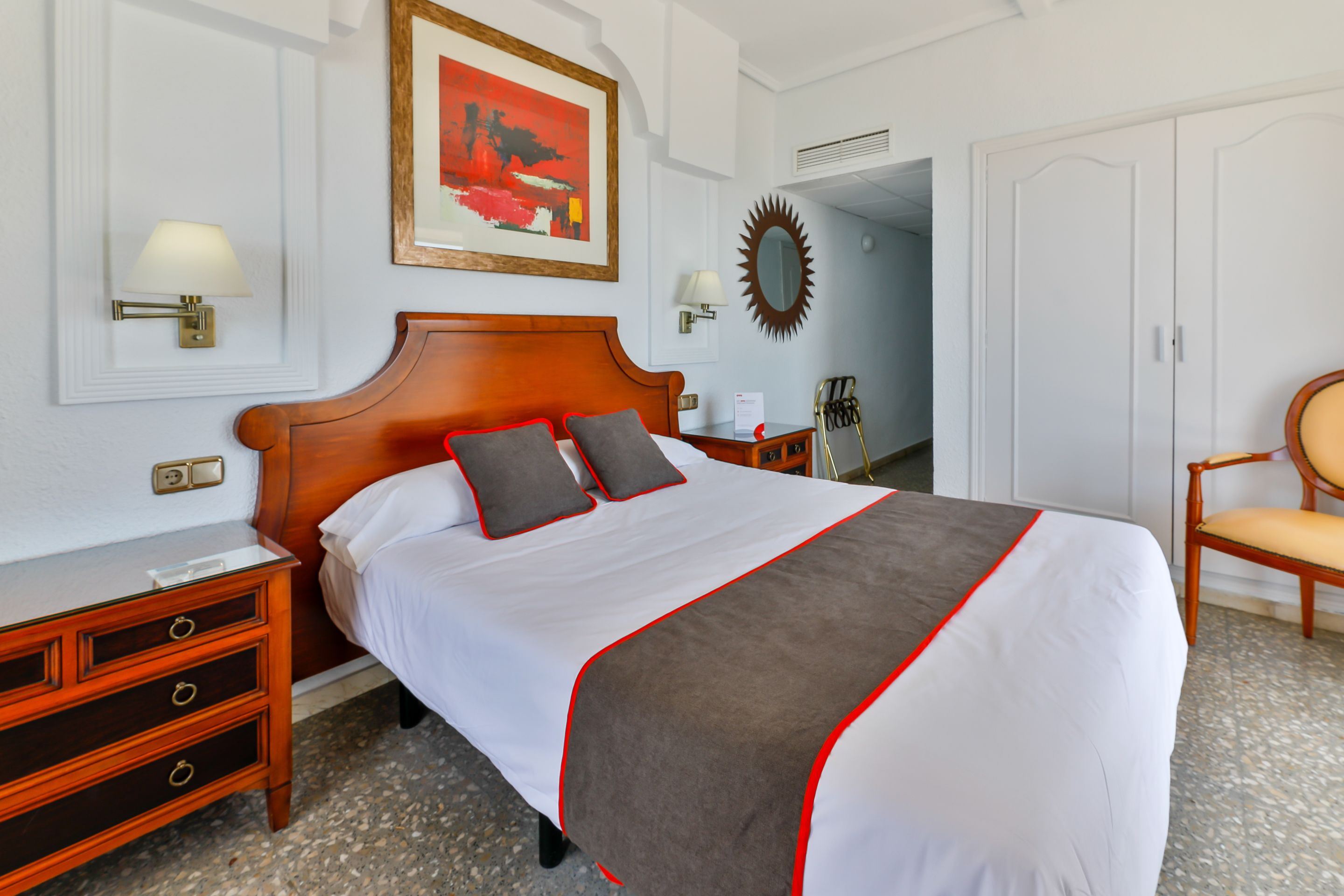Un cuarto de hotel ordenado con una cama grande, una mesita de noche de madera, una silla y un armario.