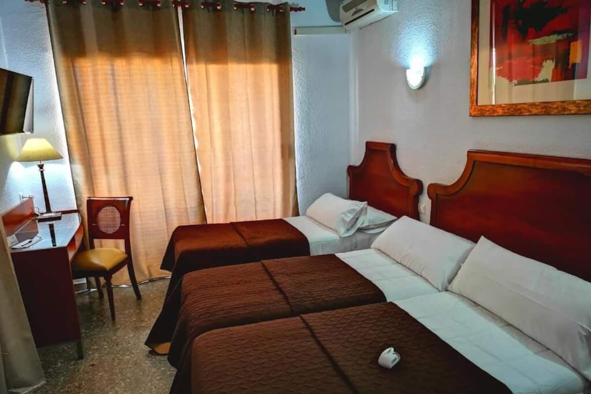 A hotel room with two beds, a desk, a chair, and a painting on the wall.