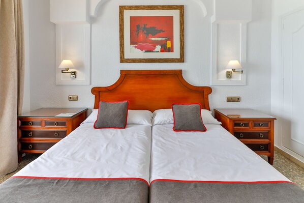 A double bed with white linens and red trim, two bedside tables with lamps, a wooden headboard, and a framed artwork above the bed. - Hotel Polamar (Santa Pola)