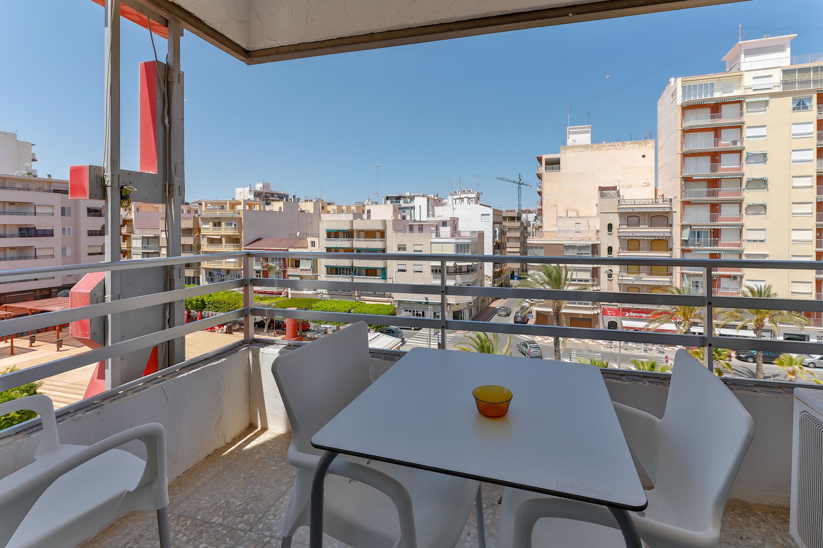 Un balcon avec une table et des chaises, donnant sur un paysage urbain avec des immeubles et une grue de construction.