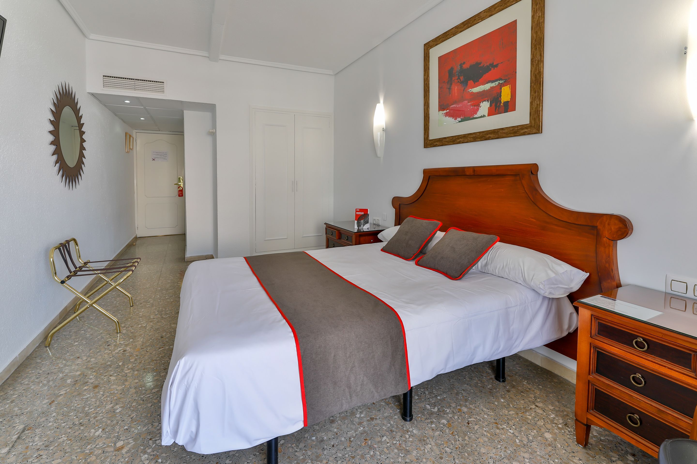 A hotel room with a large bed, a wooden nightstand, a chair, and a framed picture on the wall.