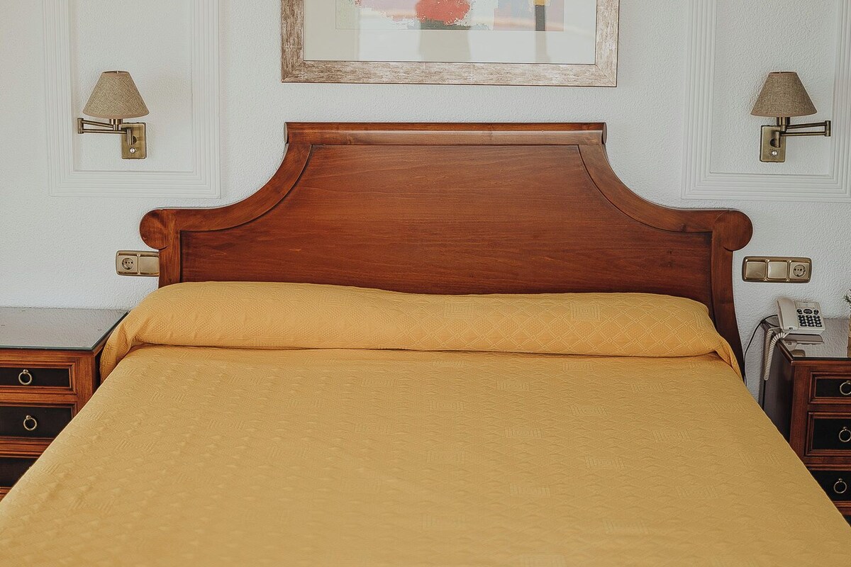 A neatly made bed with a wooden headboard, a framed picture above it, and two bedside lamps.