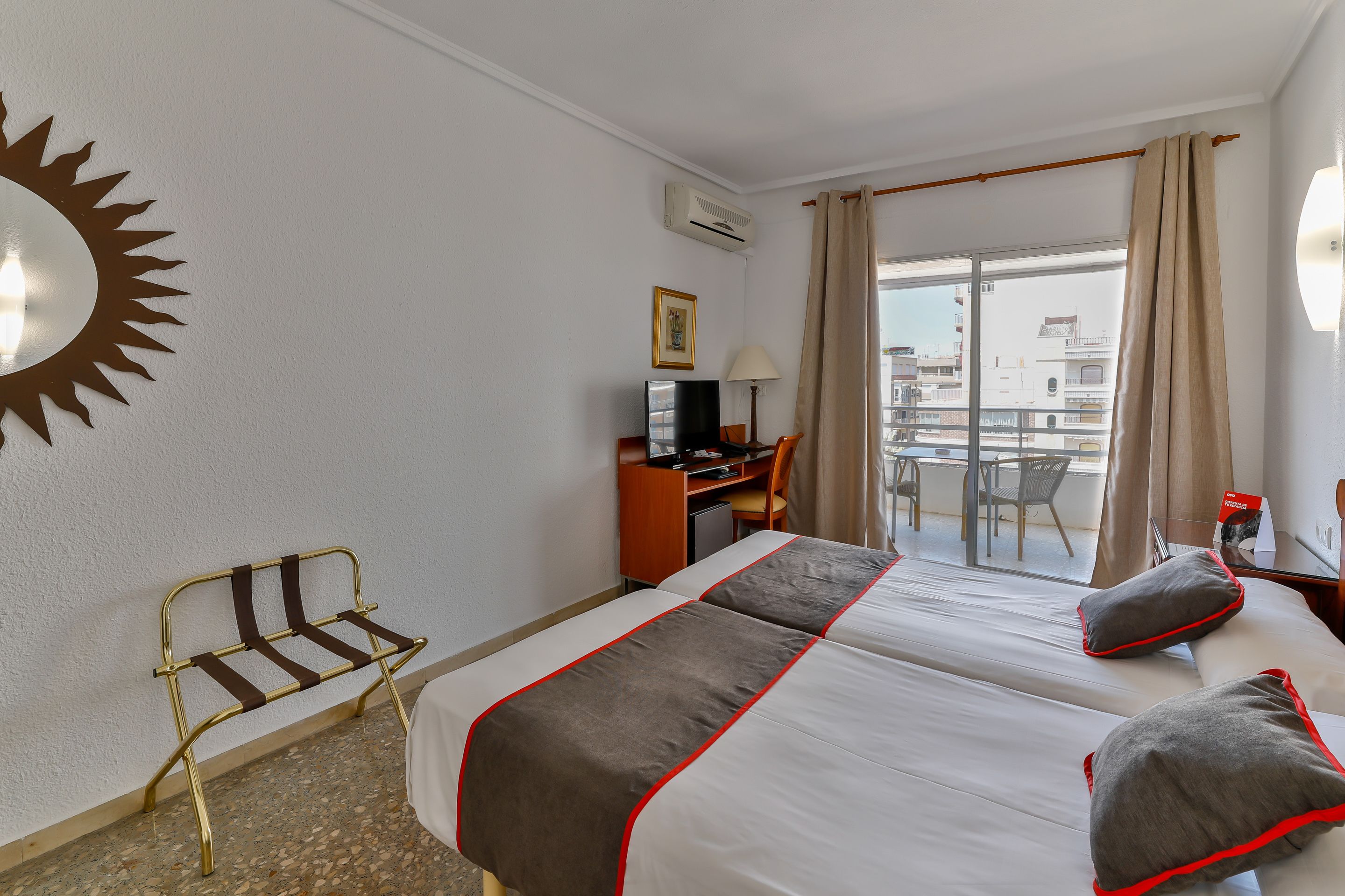 A hotel room with two beds, a desk, a chair, and a balcony with a view.