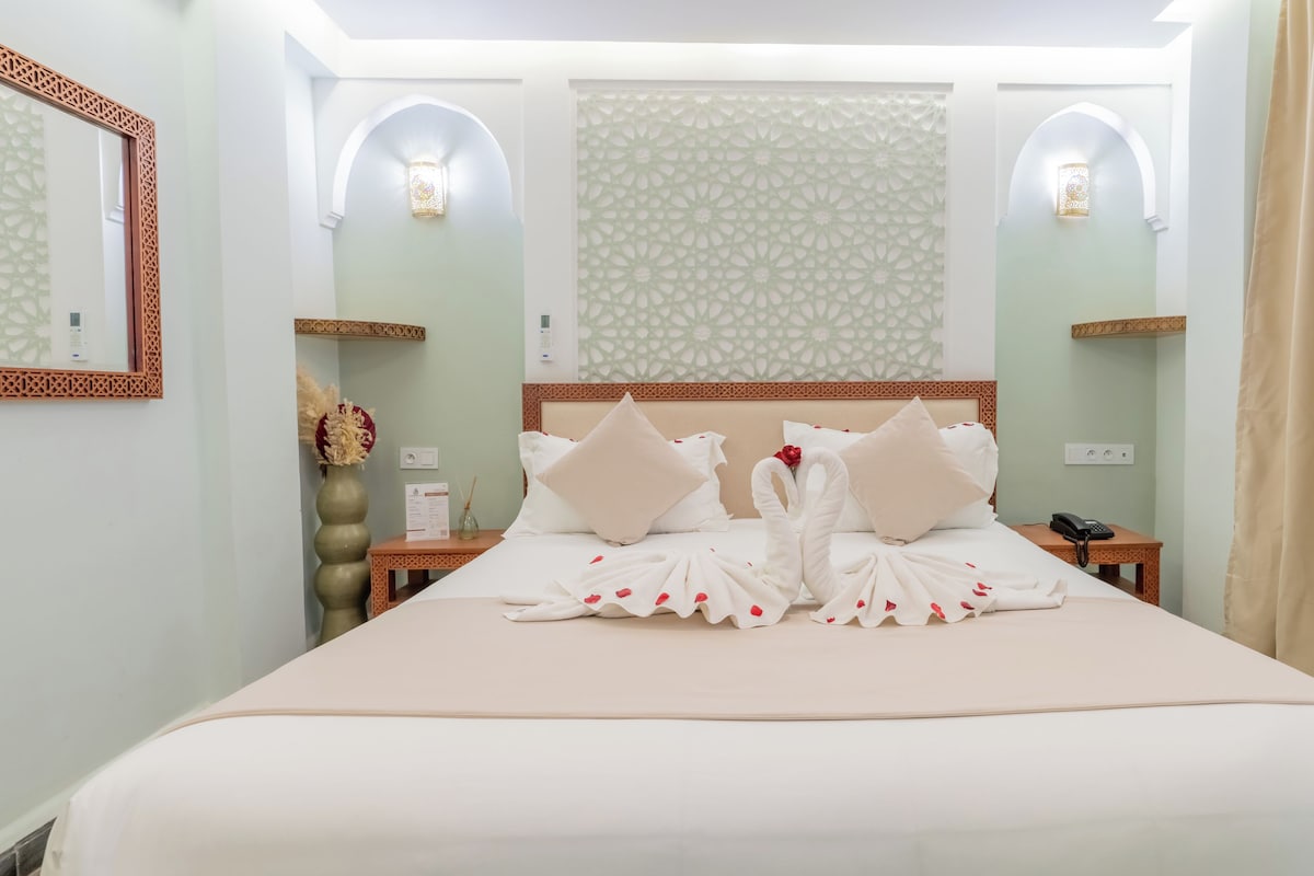 A hotel room with a large bed, two nightstands, a mirror, and decorative wall sconces.