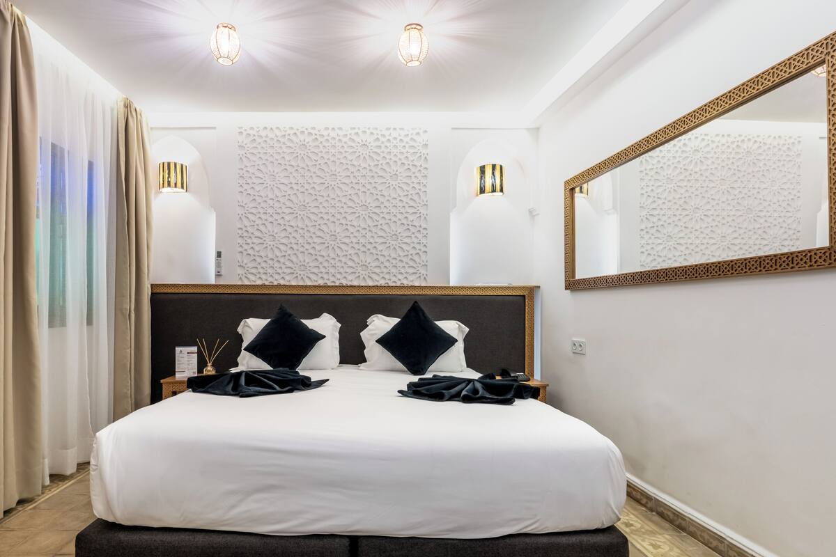 Une chambre d’hôtel avec un grand lit, deux lampes de chevet, un miroir et un panneau décoratif au mur.