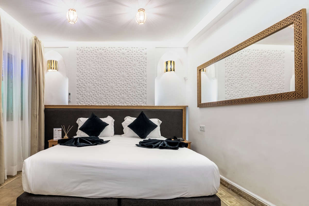 A hotel room with a large bed, two bedside lamps, a mirror, and a decorative wall panel.