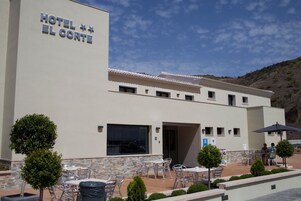Un hotel llamado "Hotel El Corte" con terraza al aire libre y fachada de piedra.