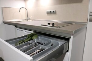 Una cocina con un lavamanos integrado, un escurreplatos y un cajón con utensilios.