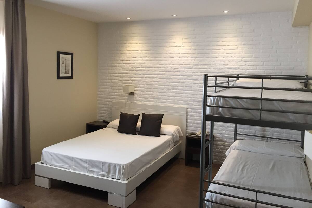 A bunk bed room with a white brick wall, a bedside table with a lamp, and a framed picture on the wall.
