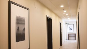 A hallway with framed pictures on the walls, doors, and a bench in the distance.