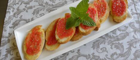 A white rectangular plate with six pieces of toast topped with tomato sauce and garnished with a mint leaf, placed on a table with a patterned tablecloth.