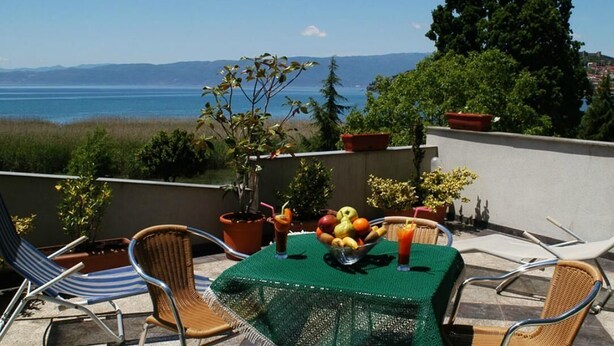 A terrace with a table set for two, a view of the sea, and potted plants.
