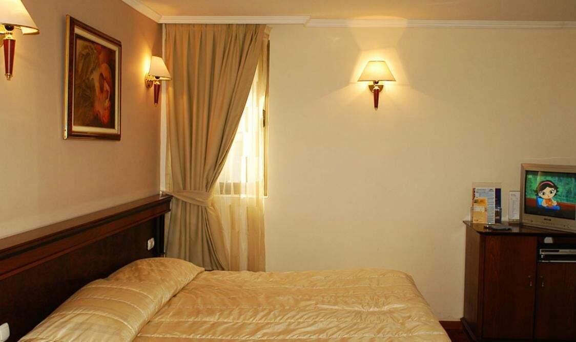 A hotel room with a bed, a television, and two wall-mounted lamps.