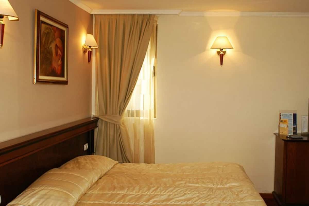 A hotel room with a bed, a television, and two wall-mounted lamps.