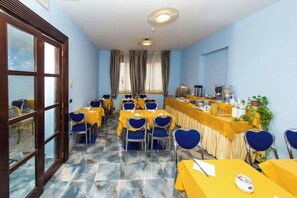 Un salón de conferencias con mesas y sillas, una zona de buffet y vistas a través de una ventana.