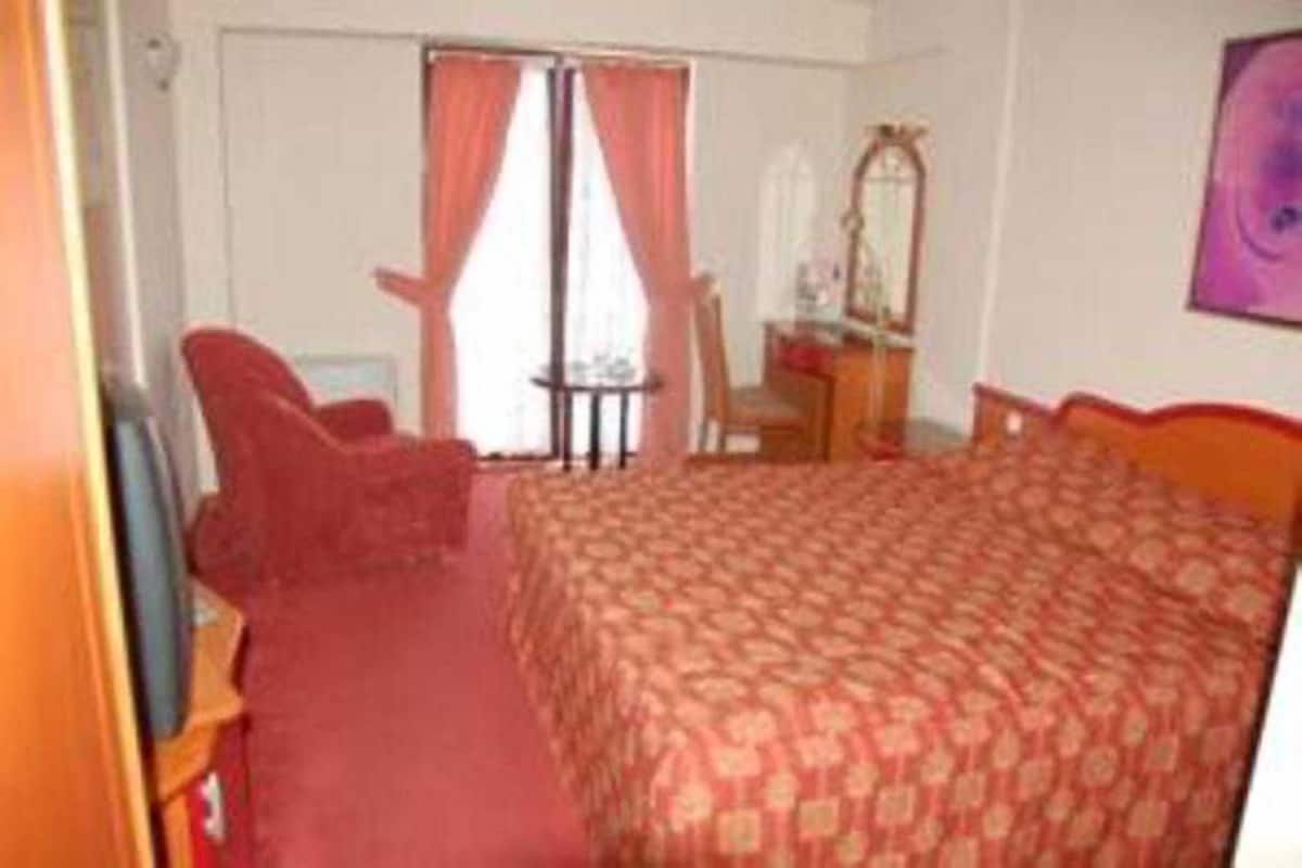 A hotel room with a bed, a chair, a small table, and a mirror.