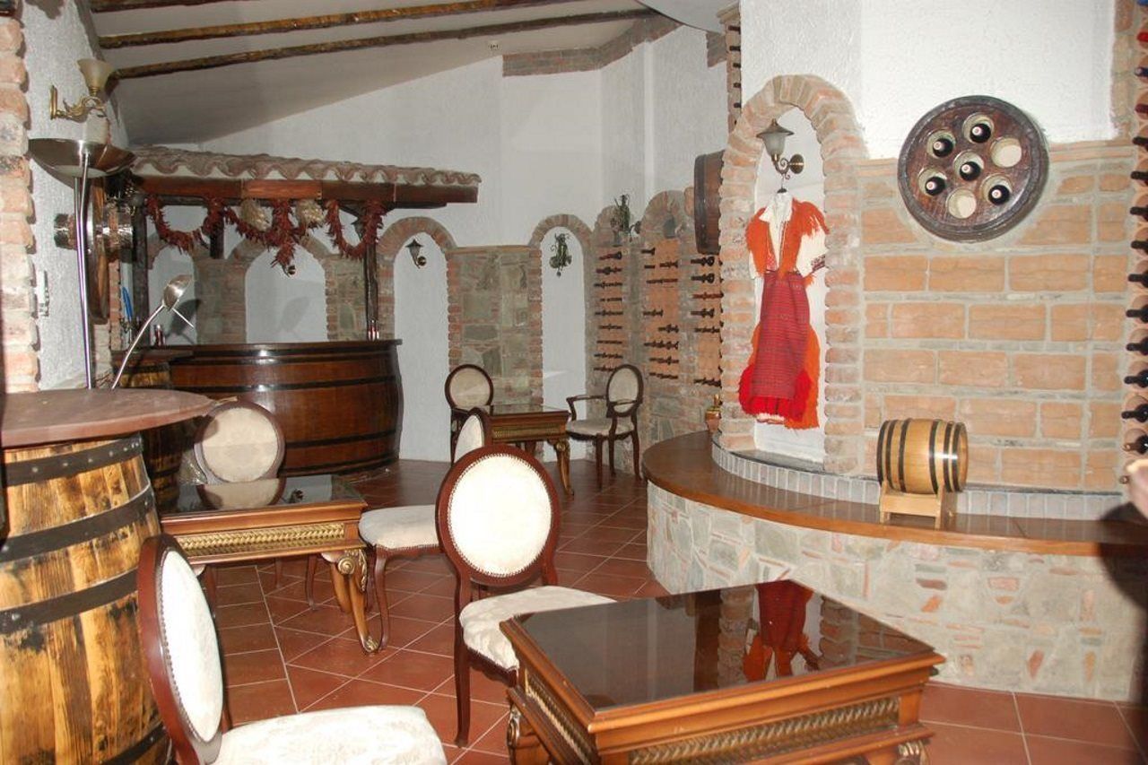 A room with a wooden bar, stone walls, and a mural of a woman. There are chairs and a table in the center.