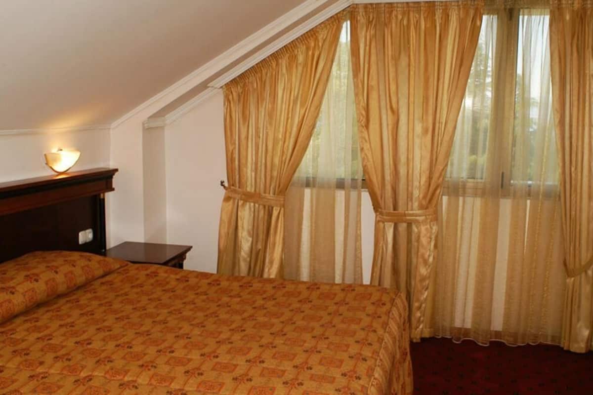A hotel room with a large bed, a nightstand, a lamp, and curtains.