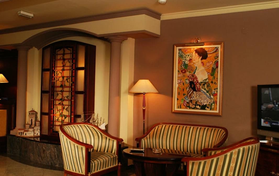 Een hotel lobby met een groot raam, twee gestreepte fauteuils, een kleine tafel, een lamp, een schilderij en een televisie.